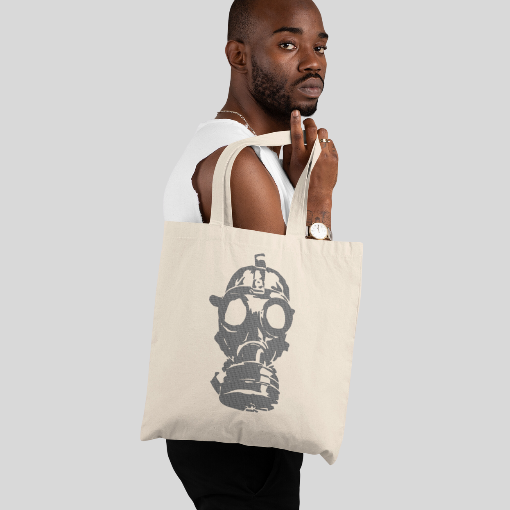 Tan canvas tote bag with large image of gray gas mask in center and handles above, against a white background.