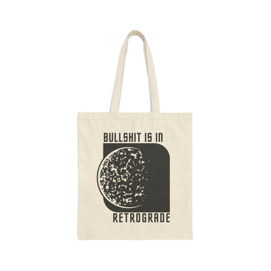 Tan canvas tote bag with "Bullshit is in Retrograde" written in a futuristic font above and below a black and white illustration of Mercury fading into a black rhombus shape and with handles above, against a white background.