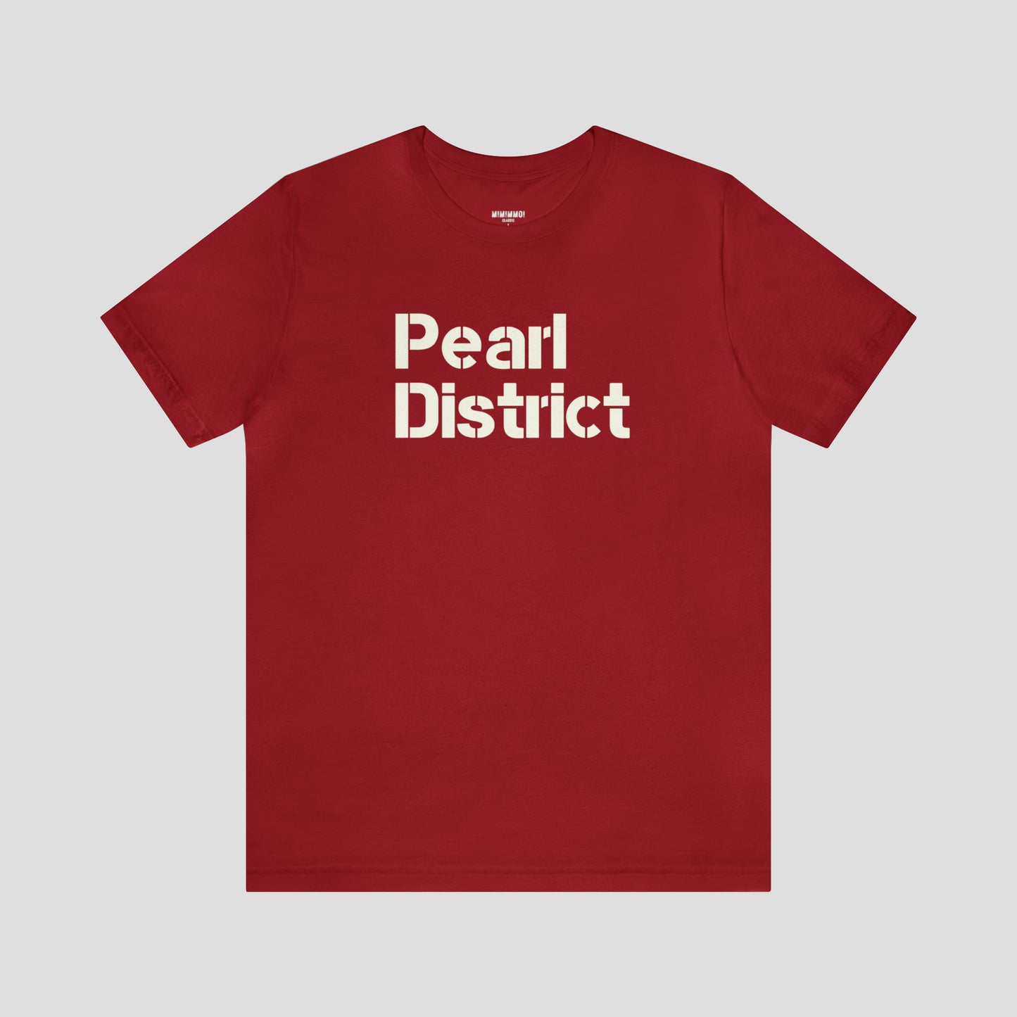 Front view of red t-shirt and large white stenciled lettering with the words Pearl District in center, against a gray background.