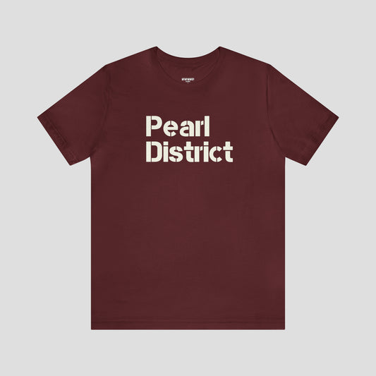 Front view of maroon t-shirt and large white stenciled lettering with the words Pearl District in center, against a gray background.