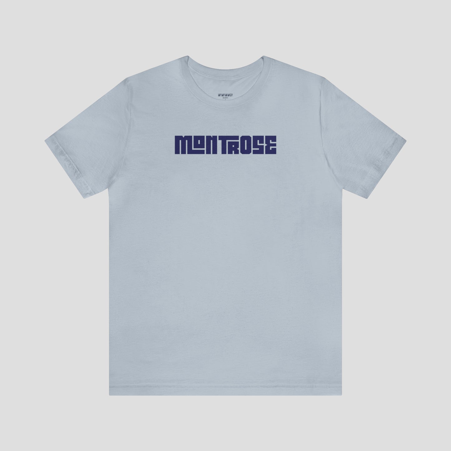 Light blue t-shirt with the word Montrose written in navy colored interlocking block letters across the chest, against a gray background.