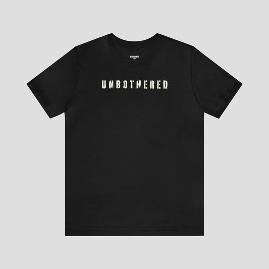 Front view of black t-shirt with the word "Unbothered" in white, distressed stenciled letters across the chest, against a gray background.