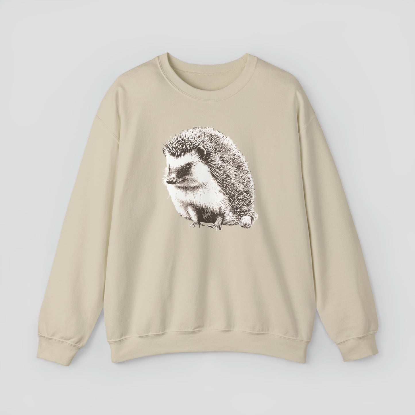 Tan colored sweatshirt with large illustrated image of white and brown hedgehog in the center, against a gray background.