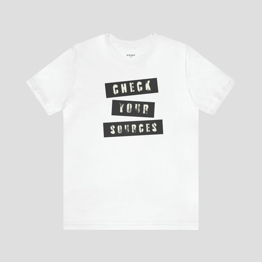 White t-shirt with "Check Your Sources" in white grunge letters set in black boxes against a light gray background.